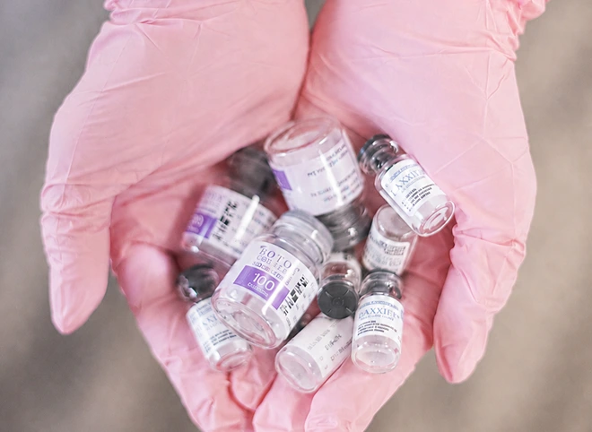 Botox and Daxxify vials held in pink-gloved hands