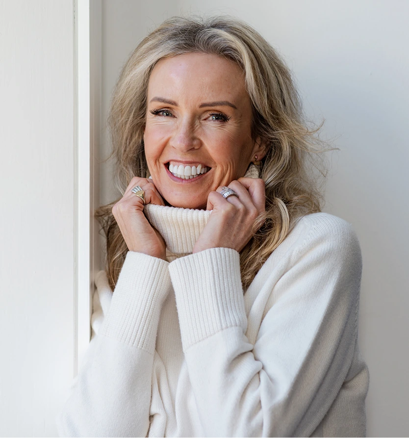 Smiling mature woman in a white sweater, representing facial volume restoration